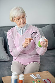 Senior woman with magnifier scrutinizing the medicines