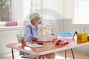 Senior Woman Making Clothes Using Sewing Machine At Home