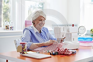 Senior Woman Making Clothes Using Sewing Machine At Home