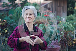 Senior woman making a heart symbol while standing in the garden. Space for text. Concept of aged people and healthcare