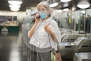 Senior woman in mask talking on phone at entrance to subway station