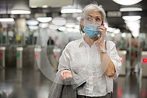 Senior woman in mask talking on phone at entrance to subway station