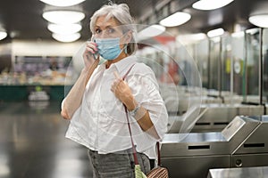 Senior woman in mask talking on phone at entrance to subway station