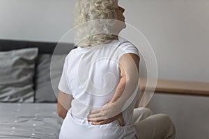 Senior woman massages her back to relieve lower back pain photo