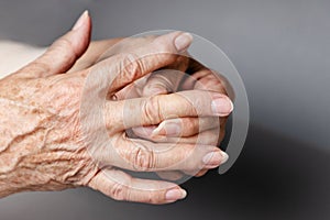 A senior woman massages her fingers, experiencing pain in the joints. Gray background, hands close-up. The concept of