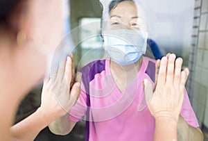 Senior woman in medical mask communicates with her daughter through the window. Elderly quarantined, isolated. Pandemic coronaviru