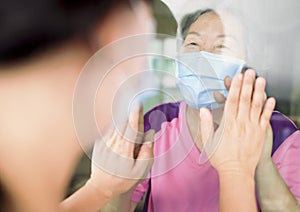 Senior woman in medical mask communicates with her daughter through the window. Elderly quarantined, isolated. Pandemic coronaviru