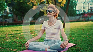 Senior woman meditating and exercising yoga lotus position outdoors. Ederly female doing stretching exercises on yoga