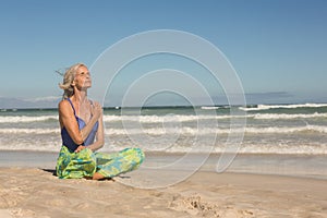 Senior woman meditating while sitting on shore against clear sky