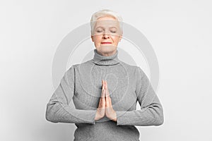 Senior woman in a meditation pose on grey background