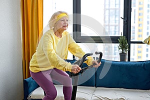 Senior woman in mid 70& x27;s exercise on stationary bike at home. Active mature female