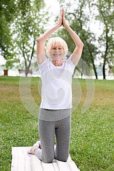 senior woman with namaste gesture practicing yoga on mat