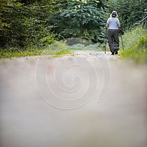 Senior woman nordic walking on a forest path