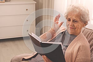 Senior woman with notebook at home, space for text. Age-related memory impairment