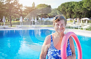 Senior woman (over age of 50) in sport goggles, swimsuit and with swim noodles near swimming pool.