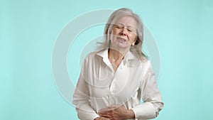 Senior Woman in Pain, Clutching Stomach with Discomfort on Teal Background
