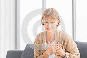 Senior woman with pain on heart in living room, Mature female presses hand to chest has heart attack suffers from unbearable pain