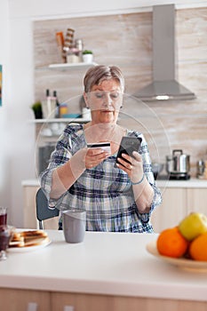 Senior woman paying online using smartphone app and holding credit card