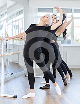Senior woman performing battement tendu at barre during group rehearsal photo