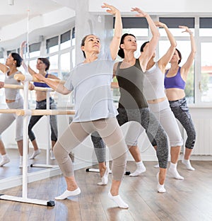 Senior woman performing demi plie at barre at fitness session