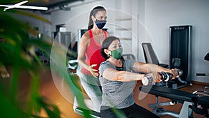 Senior woman with personal trainer doing exercise in gym, coronavirus concept.