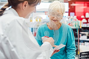 Senior woman in pharmacy talking to the chemist or pharmacist photo