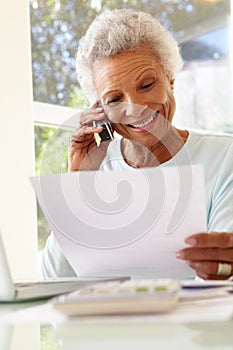 Senior Woman On Phone Using Laptop At Home
