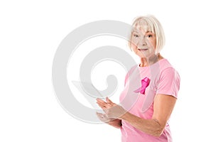senior woman in pink t-shirt with breast cancer awareness ribbon using digital tablet and looking at camera