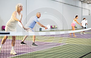Senior woman playing doubles pickleball with male partner indoors