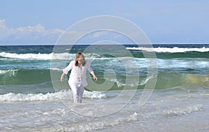 Senior woman playing sea gets surprised by cold surf wave