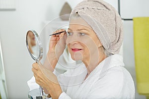 Senior woman plucking eyebrows