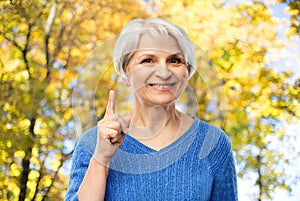 Senior woman pointing finger up in autumn park