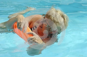 Senior donna ha il divertimento in piscina con un po ' di consiglio nelle sue mani, facendo watergynmastics per la salute.