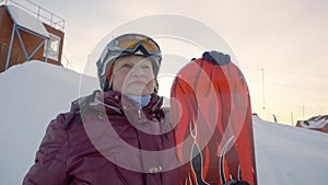 Senior woman posing with snowboard on the mountain peak.