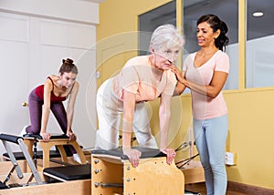 Senior woman practicing pilates on combo chair with Hispanic female trainer