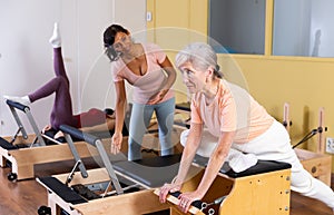 Senior woman practicing pilates on combo chair with Hispanic female trainer