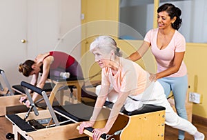 Senior woman practicing pilates on combo chair with Hispanic female trainer