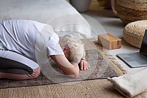 Senior woman practicing yoga at home doing balasana position