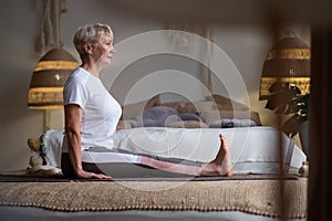 Senior woman practicing yoga, sitting in Dandasana exercise at home