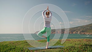 Senior woman practicing yoga in tree pose near ocean