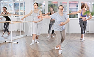 Senior woman practicng with group of female ballet amateurs in studio