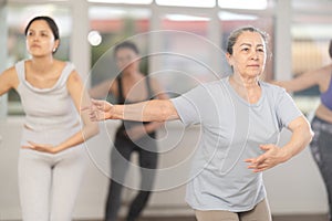 Senior woman practicng with group of female ballet amateurs in studio