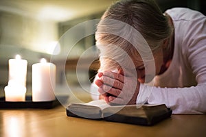 Senior woman praying, hands clasped together on her Bible.