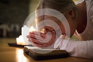 Senior woman praying, hands clasped together on her Bible.