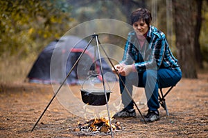 Senior woman preparing food on campfire while living