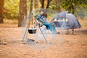 Senior woman preparing food on campfire while living in tent in forest