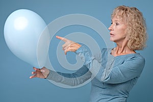 Senior woman r holding a blue balloon being alone on her Birthday party