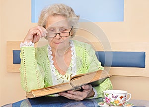 Senior woman reading a big book at home