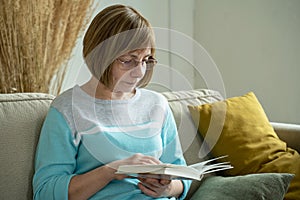 Senior woman reading a book alone at home. Middle aged senior female relaxing, enjoying free time, weekend at home