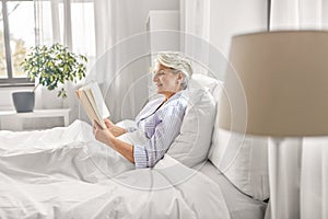 senior woman reading book in bed at home bedroom